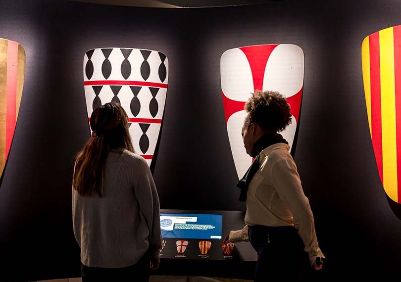 2 women standing in front of crusaders shileds inside the museum